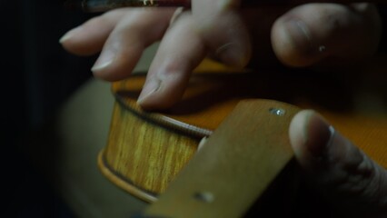 Luthier carefully applying dark varnish to handcrafted violin with soft brush, creating vintage patina in traditional wooden workshop, highlighting meticulous instrument making skill