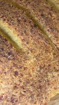 Close up of female chef cutting loaf of bread with knife on wooden board, slicing into equal parts under natural light, focus on hands guiding blade across crust and forming uniform slices