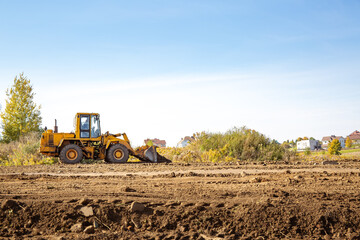 Yellow bulldozer at a construction site. Big wheel excavator leveling and clearing the land plot side view. Moving earthworks soil. Copy space. Building area. Special transport. High quality photo. © Hanna