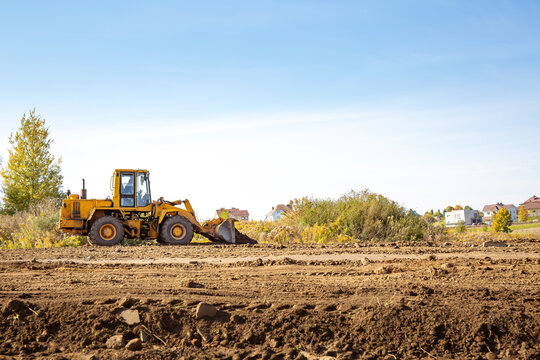 Yellow bulldozer at a construction site. Big wheel excavator leveling and clearing the land plot side view. Moving earthworks soil. Copy space. Building area. Special transport. High quality photo.