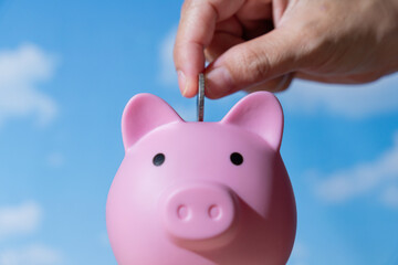 A hand is dropping a coin into the slot of a pink piggy bank. Saving money, financial concept.