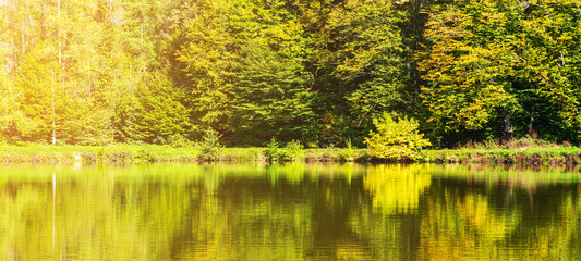 landscape with trees reflected in the lake water on a sunny autumn day