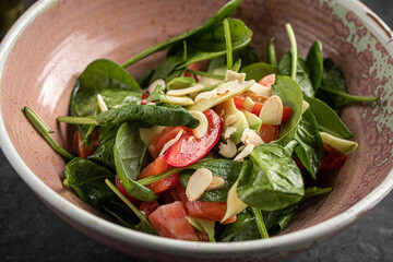 Fresh spinach salad with salmon, almonds and vegetables in ceramic bowl