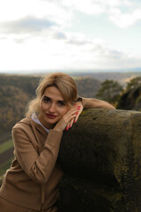 Woman in a beige outfit walking through a natural park with beautiful green cliffs on a cloudy day. Serene moment, connection with nature, stylish outdoor lifestyle.