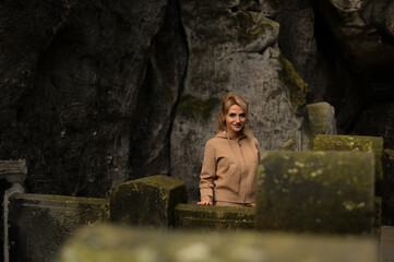 Woman in a beige outfit walking through a natural park with beautiful green cliffs on a cloudy day. Serene moment, connection with nature, stylish outdoor lifestyle.
