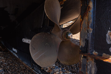 The rusty propeller of a boat docked on a beach.