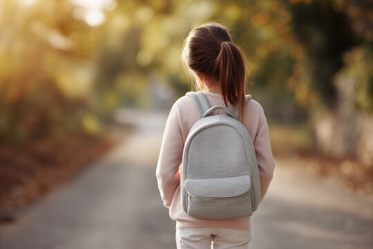 Young girl with backpack walking on path. Back to school, outdoor setting, natural light, neutral colors, childhood innocence, and adventure.