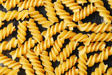 Yellow fusilli pasta background. Uncooked spiral noodles closeup. Italian raw food texture. Dry...