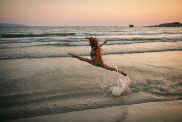a slender sporty girl in a beautiful swimsuit at the sunset of a summer day on the sea coast. beautiful long haired blonde at the beach