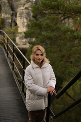 Young woman in a white puffer jacket walking through a beautiful green natural park on a sunny day....