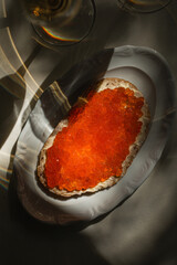 Bread with red caviar and butter on white plate in dramatic light