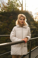 Young woman in a white puffer jacket walking through a beautiful green natural park on a sunny day. Outdoor lifestyle, peaceful moment, nature and fashion concept.