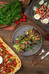 Meat salad with greens plum and pine nuts on gray plate