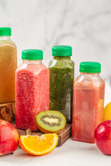 Red smoothie in plastic bottle with kiwi and orange on white table