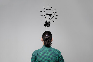 A woman is staring at a wall with a drawing of a light bulb. Idea and thinking concept