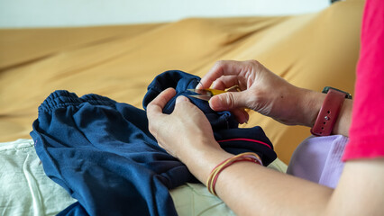  A mother hand-sewing trouser legs, fixing worn pants for her child with gentle hands