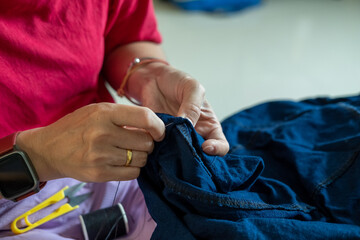 Caring mother repairing her child&rsquo;s trousers by hand, focusing on sewing trouser legs.