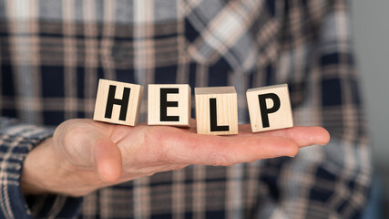 A person is holding a wooden block with the word HELP written on it