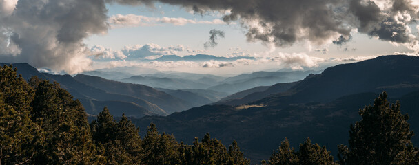 Dramatic layered mountain landscape under thick cloud cover with sunlight breaking through