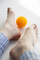 Close-up of flat feet with bunions and yellow massage ball on white background.