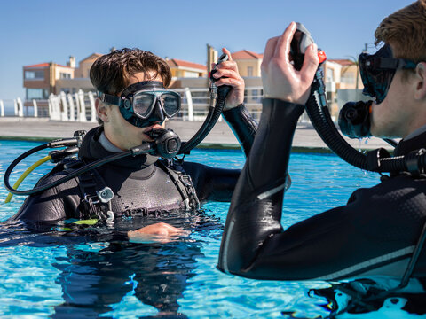 Close-up of two scuba divers in a pool at a dive resort practicing skills, holding their inflator hoses up and their regulators in their mouths. Getting ready to submerge.