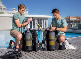 Two scuba divers wearing summer clothes are getting their gear ready next to a pool at a dive...