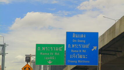 Clear green expressway sign pointing toward Don Mueang and Chaeng Wattana, set against a partly cloudy sky above Bangkok roadways.