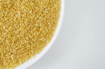 Raw bulgur wheat grains in a white plate on a gray background. Healthy eating concept. Vegan and vegetarian food. Horizontal orientation. Top view. Copy space