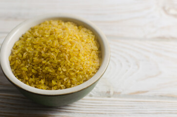 Raw bulgur wheat grains in a ceramic green bowl on a white wooden table. Healthy eating concept. Vegan and vegetarian food. Diet. Rustic style. Horizontal orientation. Copy space