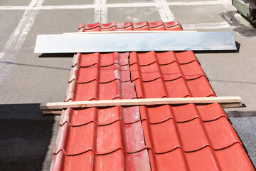 Rooftop under repair featuring red roofing sheet with metal panel and wooden plank placed over for...