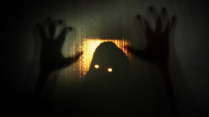 Silhouette of a hooded man with glowing burning eyes and eerily raised hands behind a transparent curtain. Concept of demons, paranormal phenomena, ghosts, zombies.
