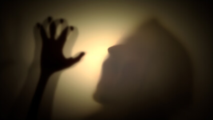 Silhouette of a hooded man with his hands raised menacingly behind a transparent curtain. Concept...