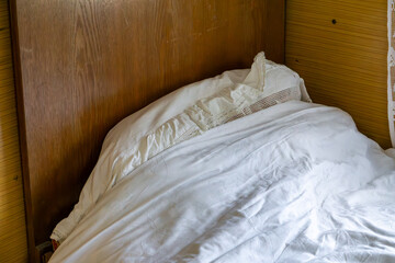 Old wooden bed with white linen and a lace pillow in a rustic interior.