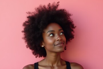 Black woman with afro hair posing in front of a pink wall looking away