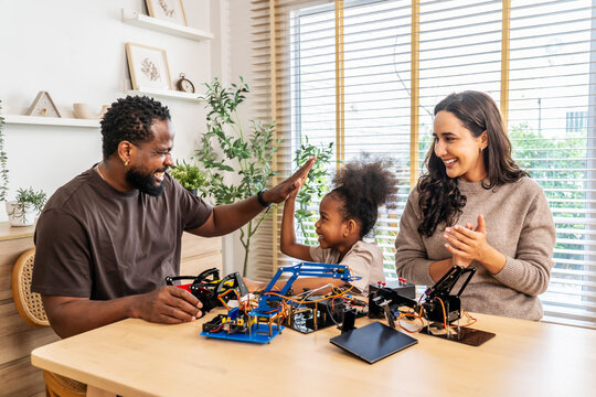 Happy african american father, mother, and daughter cheering with excitement after successfully building a robotic, enjoying a fun and educational activity together, fostering creativity - Powered by Adobe