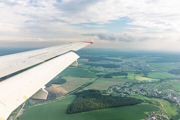 View of airplane wing, blue skies and green land during landing. Airplane window view.
