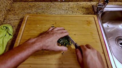 Mature male chef demonstrating precise knife skills while chopping fresh green vegetables in slow motion, representing mindful plant based culinary preparation and healthy lifestyle