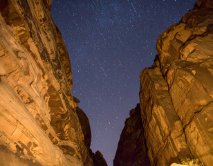 Star trails streak across the night sky above towering rock formations in a dramatic canyon view, highlighting the beauty of nature at night.