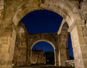 Ancient stone arches illuminated under a starry night sky, showcasing historical architecture and timeless beauty.