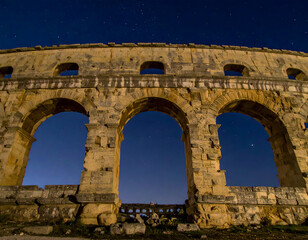 Ruins of a majestic Roman-style structure glow under the stars, highlighting the grandeur and endurance of ancient architecture in silence.
