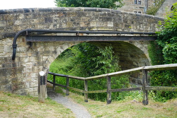 Codnor, Derbyshire, England - July 16 2025: Stone arch footbridge covered in lush vegetation.