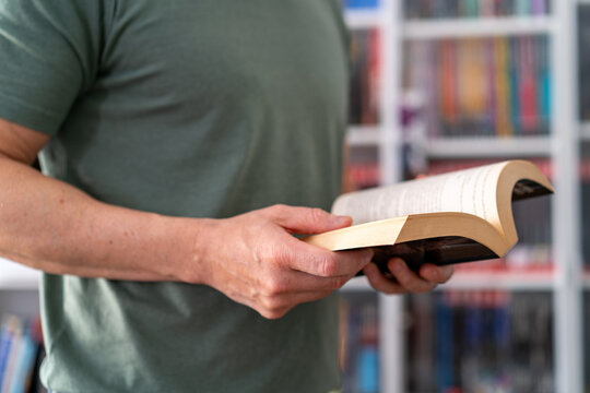 A man reads a book with a soft focus on the pages and holding the book open. - Powered by Adobe