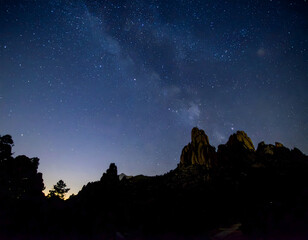 Stunning Milky Way galaxy glowing above rocky cliffs as twilight fades, blending night sky brilliance with dramatic natural silhouettes.