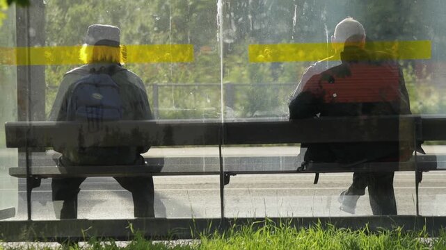 Two men are sitting at bus stop. View from back