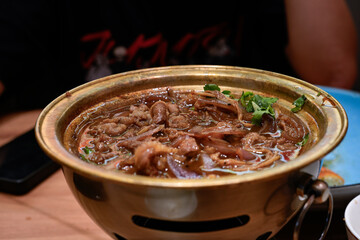 A variety of fresh ingredients, including beef, vegetables, mushrooms, and tofu, simmering in a flavorful broth