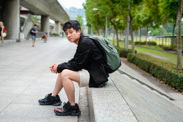 young man sitting outdoors with backpack on urban street