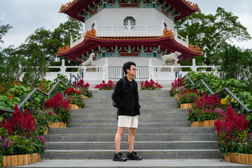 A young Asian man stands on the steps leading up to a multi-tiered traditional Chinese pagoda