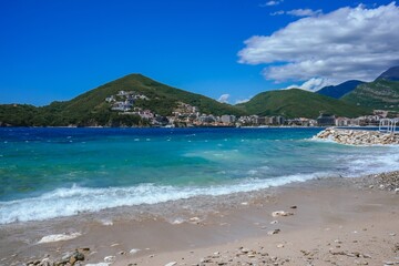 Azure Sea with Gentle White Waves, Mountains and Cloudy Sky Background in Montenegro