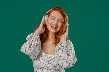 Red-haired pretty woman gets high,listening music with headphones, green studio
