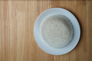 flat lay top view shot of streamed white Thai's jasmine rice in the white clean dish isolated put on the wooden plate dinner table closed to one conner of the photo with empty copy space for texts